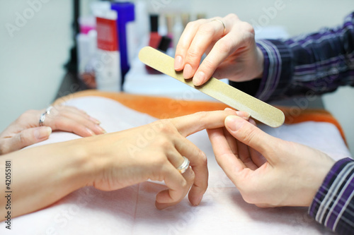 Manicurist hands make manicure by nailfile for woman in salon