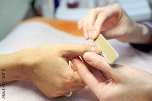 Female hands make manicure by nailfile for woman in beauty salon
