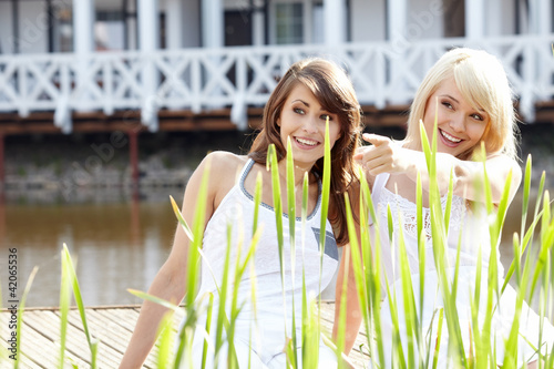 Two youngl pretty women in a park one of them points at somethin photo