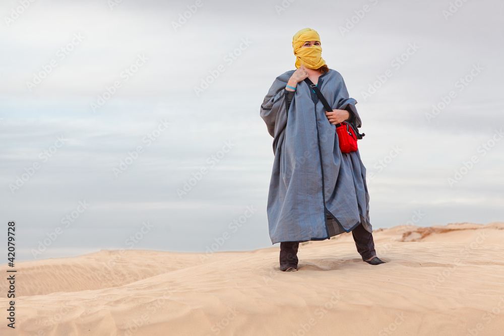 Woman in bedouin clothes standing on dune in desert Stock Photo