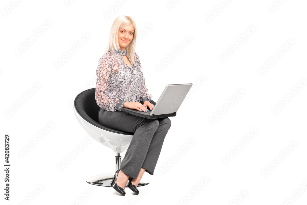 A blond woman sitting on a chair and working on a laptop