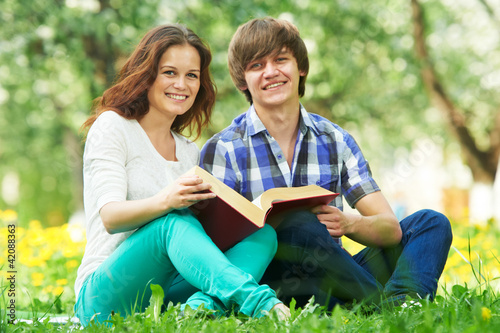 two smiling young students outdoors with book