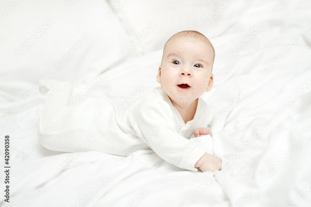 Happy active baby lying on stomach over white bed.  Three month