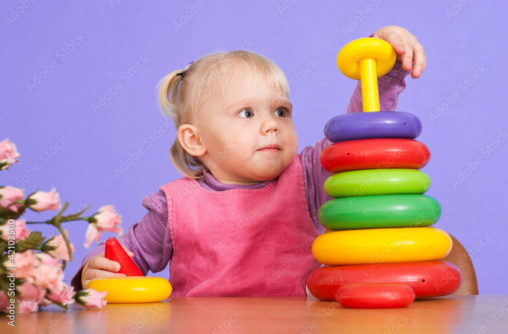 A small charming Caucasian tot sitting at the table and plays wi A small charming Caucasian tot sitting at the table and plays wi