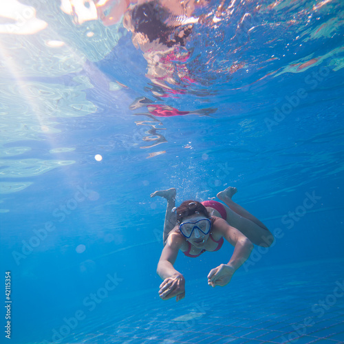 Underwater swimming: young woman swimming underwater in a pool