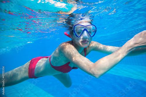 Underwater swimming: young woman swimming underwater in a pool