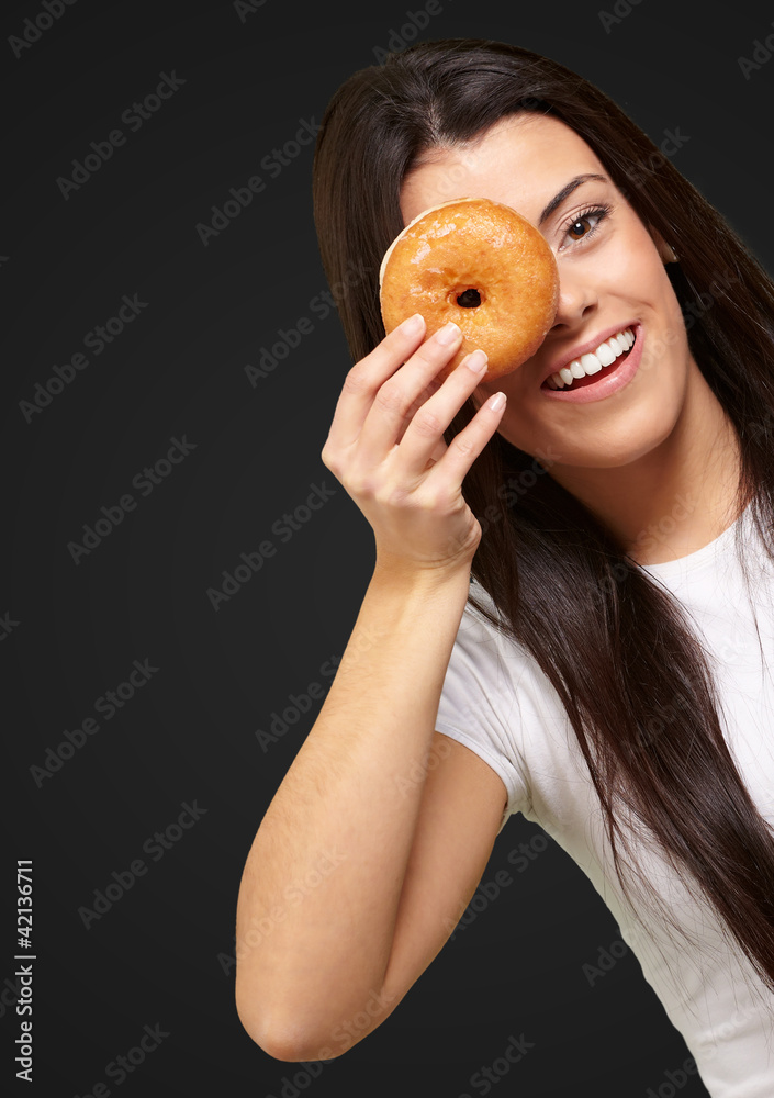 portrait of young woman looking through a donut over black portrait of young woman looking through a donut over black