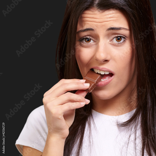 portrait of young woman eating chocolate bar over black backgrou