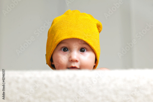 Cute Baby with a Beanie Hat behind a Sofa