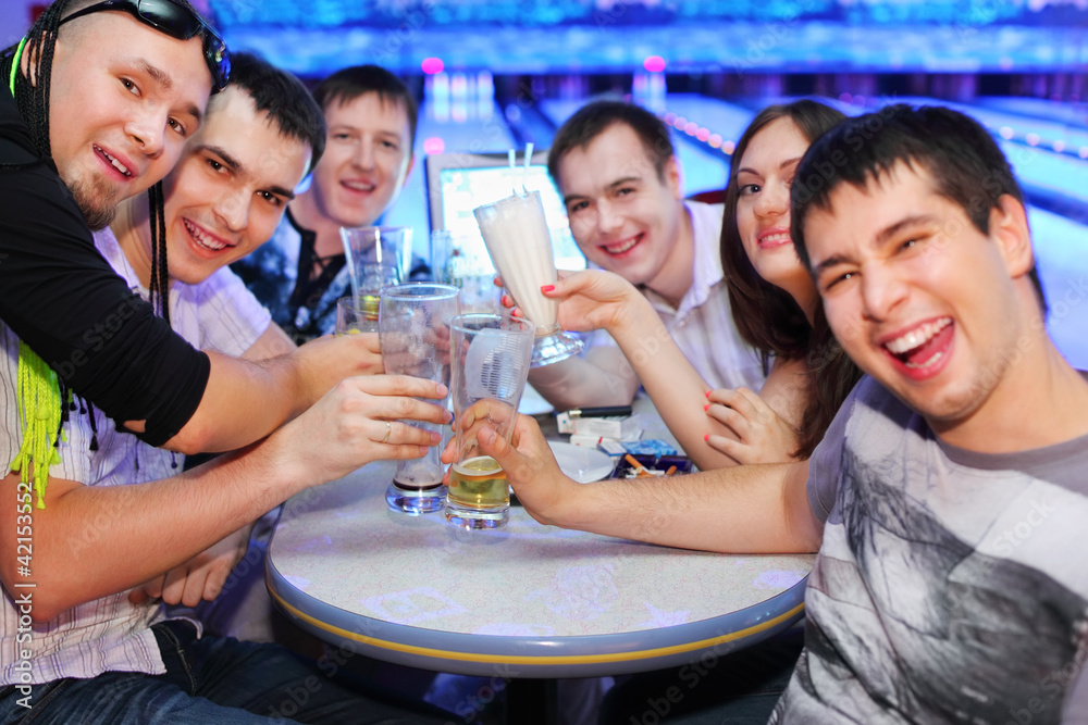 Company of happy friends sit at table and drink beer in bowling;