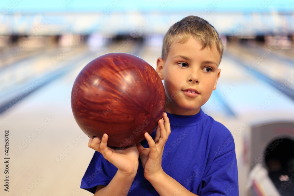 Fototapeta premium thinking boy dressed in T-shirt holds ball in bowling club
