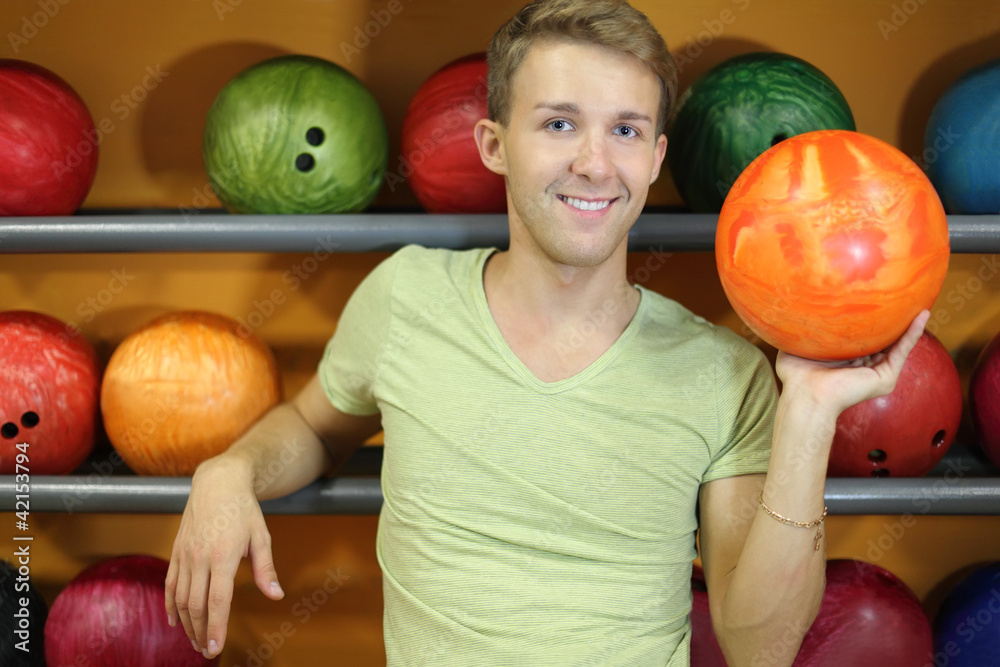 Fototapeta premium Happy man stands near shelves with balls and holds orange ball