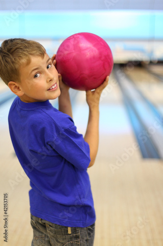 Smiling boy dressed in blue T-shirt holds ball in bowling club