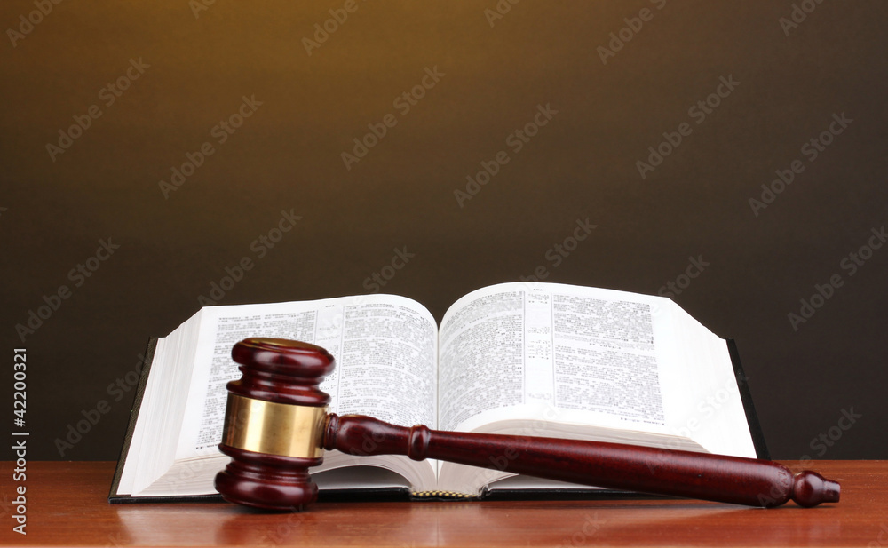 Judge's gavel and open book on wooden table on brown background
