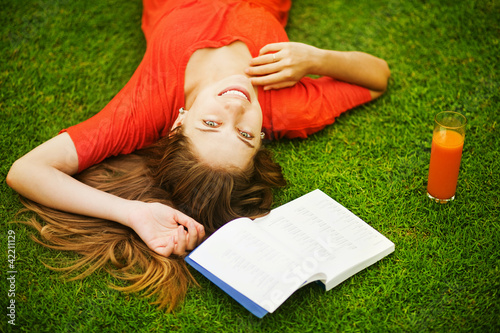 Young woman on the grass with book and orange juice