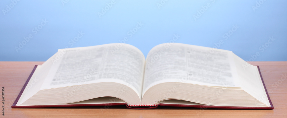 Fototapeta premium Open book on wooden table on blue background