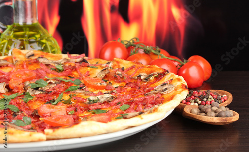 delicious pizza and tomatoes on wooden table on flame background
