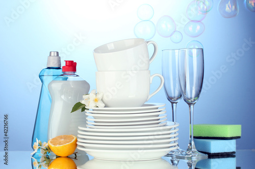 plates, glasses and cups with cleaning liquid on blue background © Africa Studio