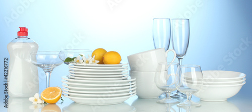 plates, glasses and cups with cleaning liquid on blue background