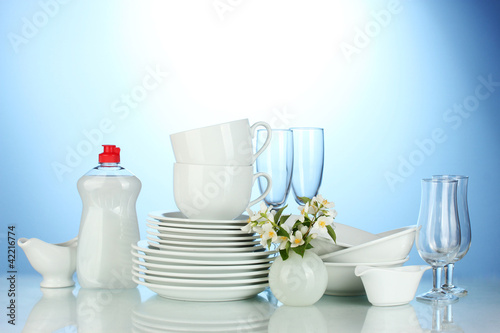 plates, glasses and cups with cleaning liquid on blue background