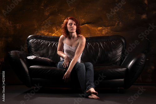 Eine junge Frau mit sichtbaren Nippeln auf schwarzem Ledersofa sitzend