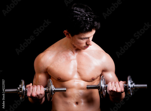 Young muscular man lifting weights on black background