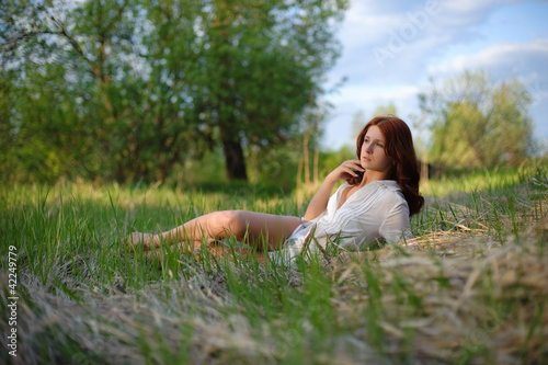 A beautiful girl with red hair lies in the grass