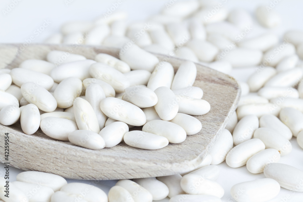 White beans on wooden spoon and a white background