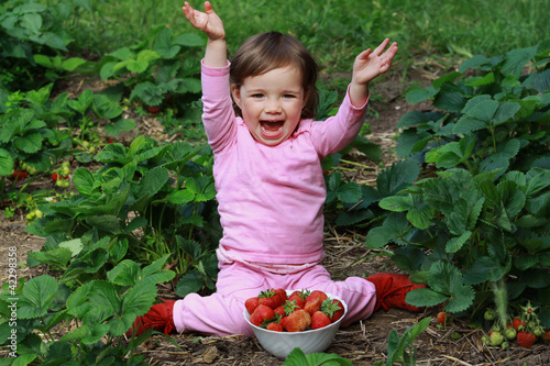 Kleinkind sitzt in einem Erdbeerbeet