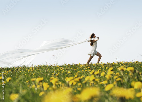 A young woman holding a white blanket in a flowerish field