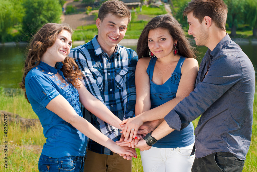 Group of four teenagers shaking hands and smiling outdoors Group of four teenagers shaking hands and smiling outdoors