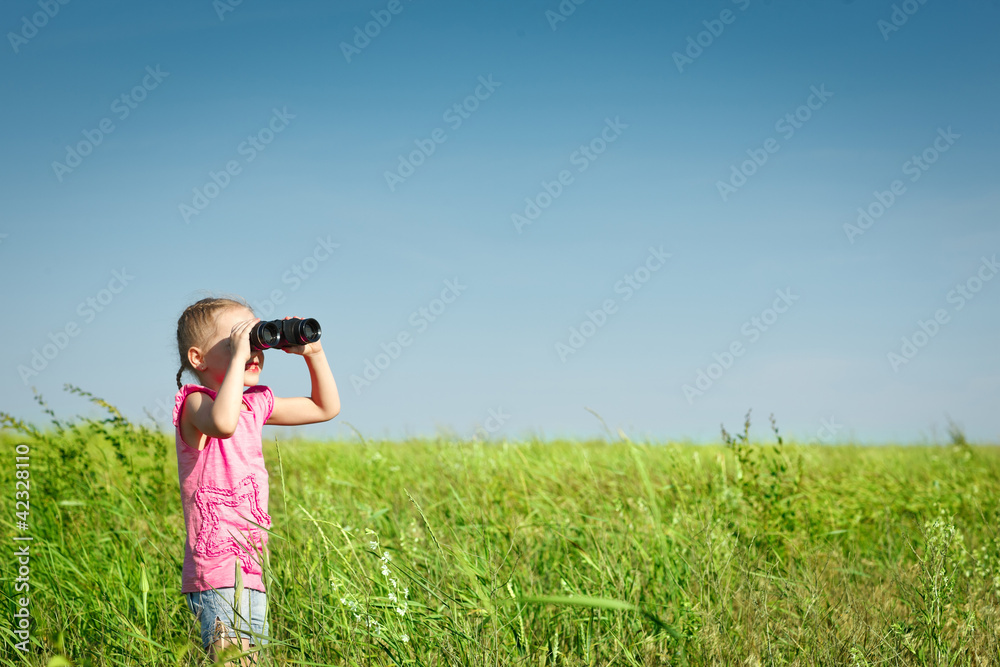 Little girl in the field looking away through binoculars