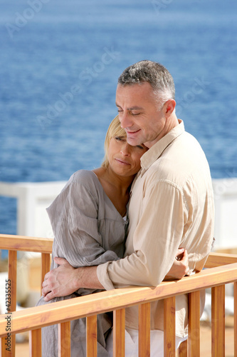 Middle aged couple stood on balcony overlooking the sea