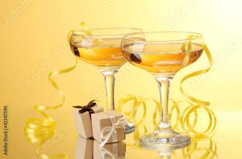 glasses of champagne, gifts and streamer on yellow background photo