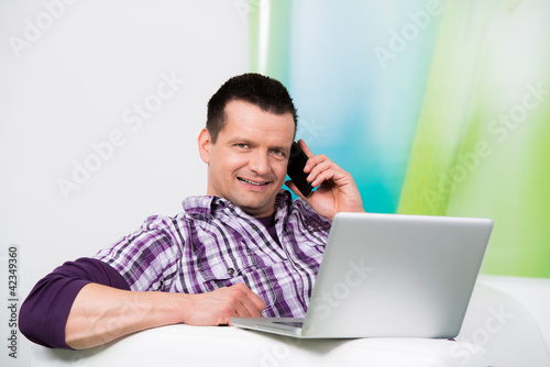 attraktiver mann sitzt am laptop und telefoniert