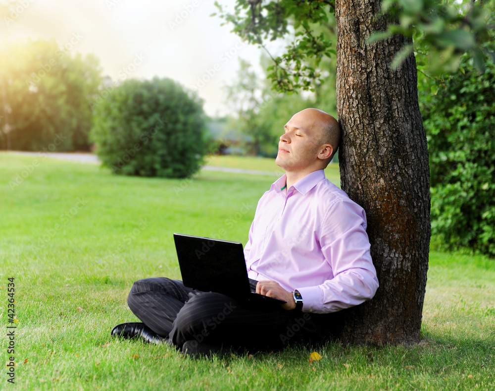 Businessman with laptop sitting near a tree Businessman with laptop sitting near a tree