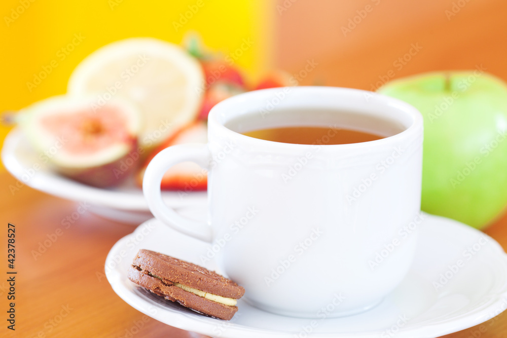 cup of tea,cookie,apple, lemon, fig and strawberries on a plate