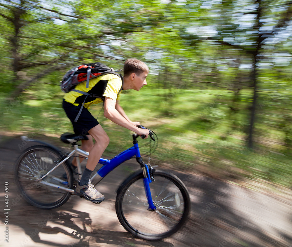 A teenager on a bicycle traveling in the forest