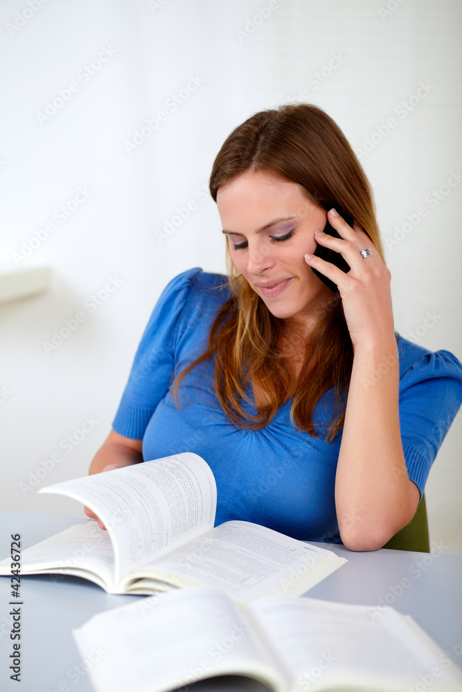 Blonde girl on cellphone while browsing a book Blonde girl on cellphone while browsing a book