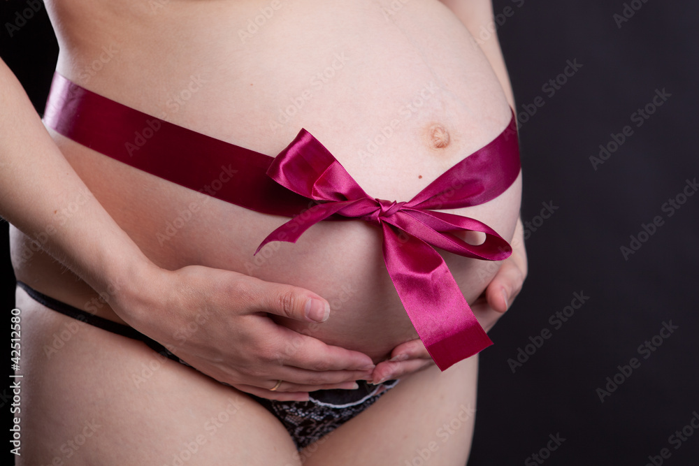 Pregnancy. Abdomen. Red Ribbon. Black background Pregnancy. Abdomen. Red Ribbon. Black background