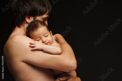 Father holding newborn baby over black background