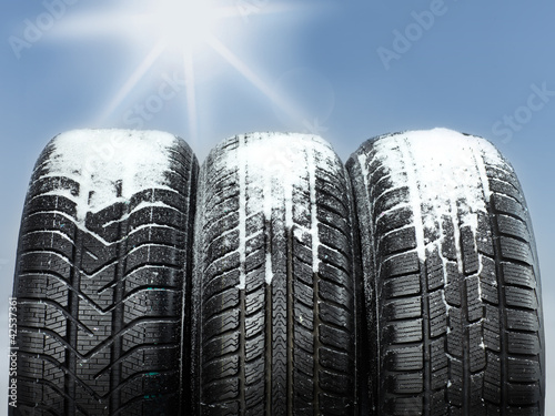 Three snowy winter tyres in front of blue sky with sunlights photo