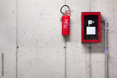 A fire extinguisher and a fire-hose on concrete wall
