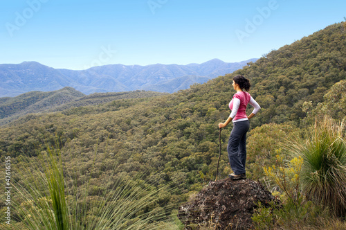 Single female hiker looks out at view in Mount Kaputar with forest below her in outback Australia