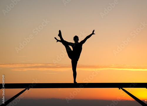 silhouette of female gymnast on balance beam in sunset