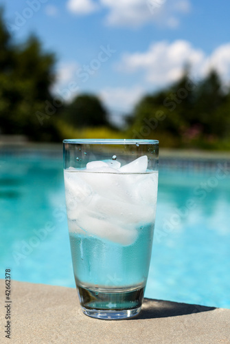 Glass of water with ice cubes on side of pool