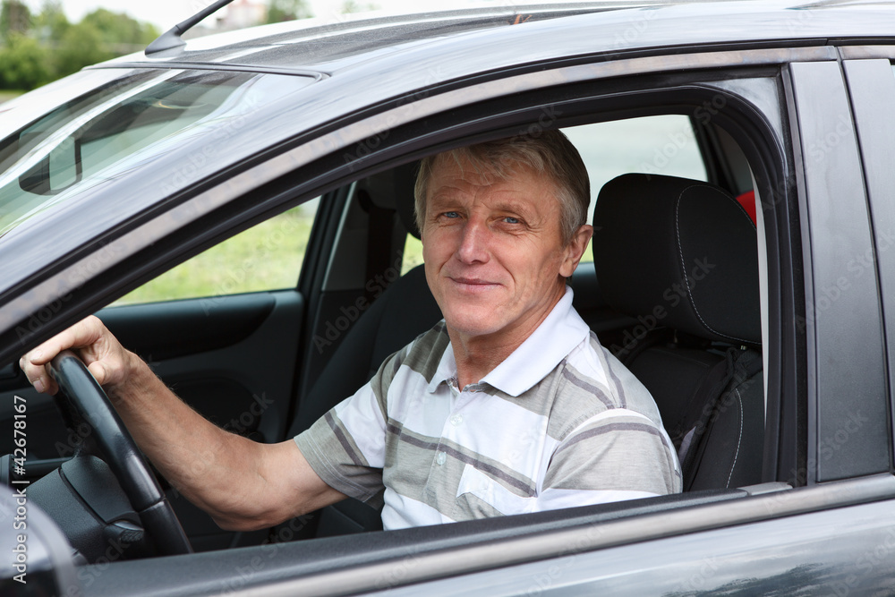 Handsome senior person sitting in car on driver seat