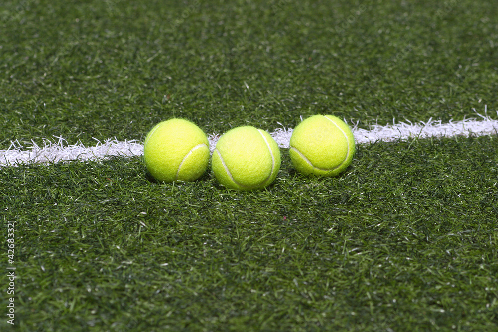 Three yellow tennis balls lays on grass court line