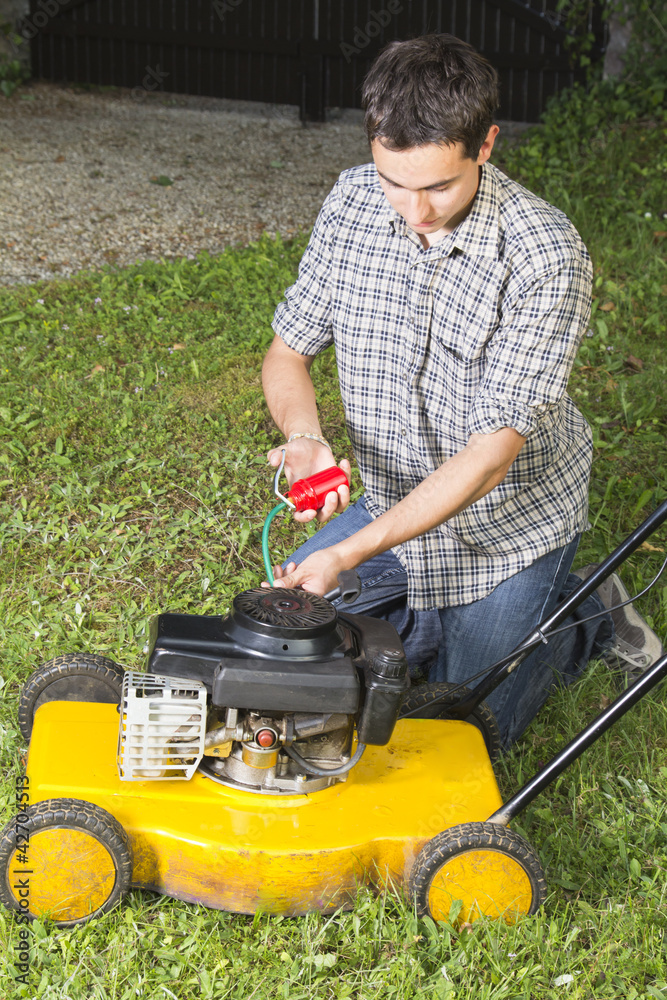 Fototapeta premium Man oiling and repairing yellow lawn mower