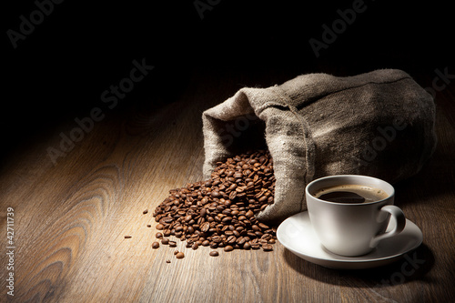 Coffee cup with burlap sack of roasted beans on rustic table #42711739